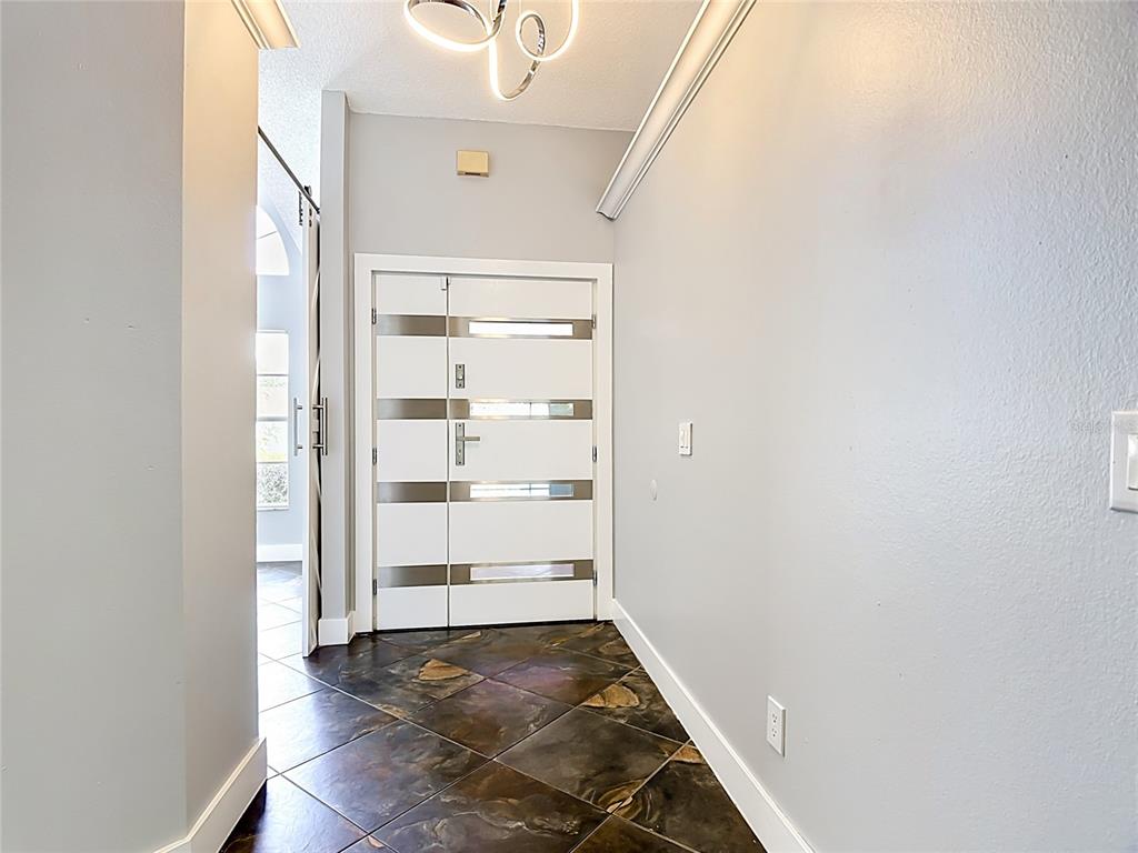A foyer features a modern white front door, dark tiled flooring, and a contemporary light fixture — 3247 TIMUCUA CIRCLE, ORLANDO, FL