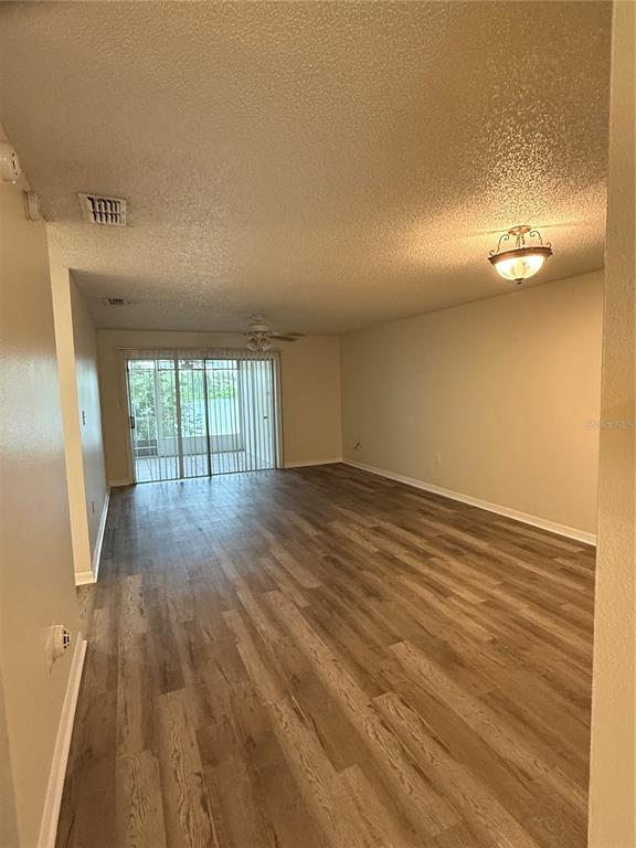 An empty living room features wood-look flooring, a ceiling fan, and sliding glass patio doors — 702 COUNTRY LANE NE UNIT 702, WINTER HAVEN, FL
