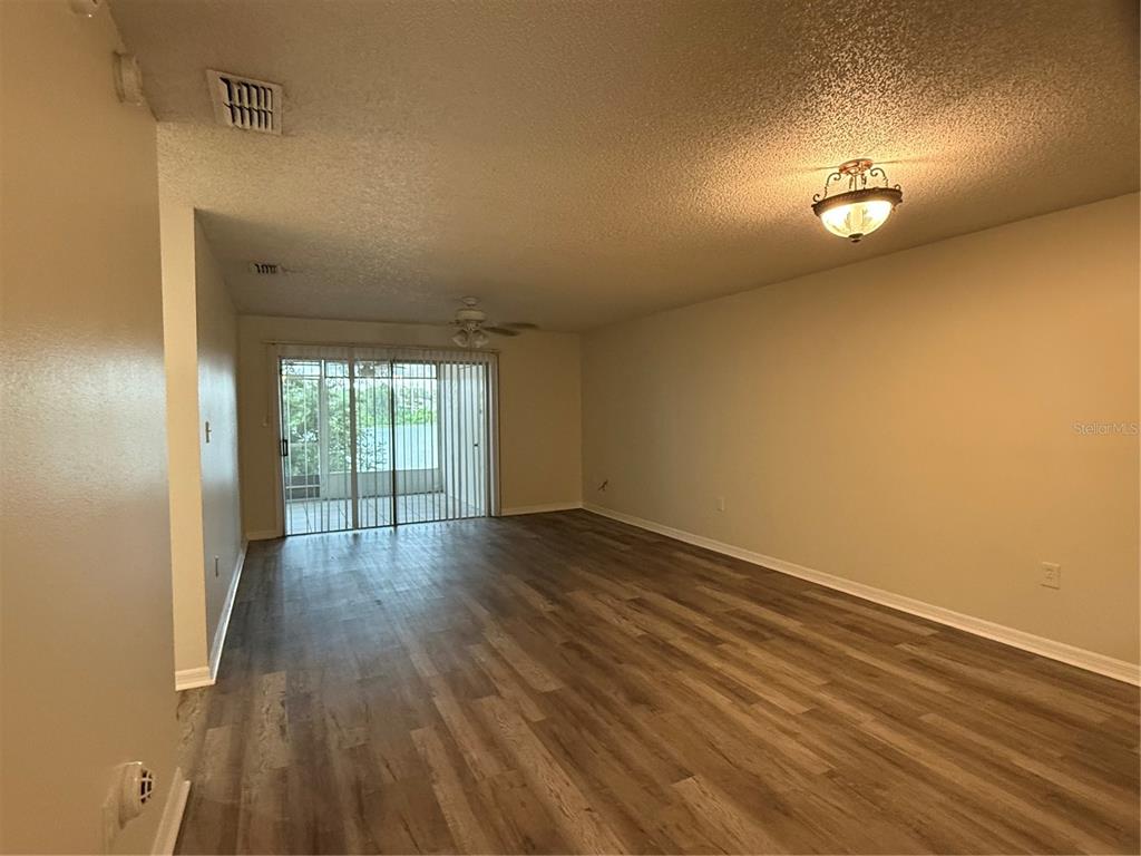 An empty living room features wood-look flooring, a ceiling fan, and sliding glass patio doors — 702 COUNTRY LANE NE UNIT 702, WINTER HAVEN, FL