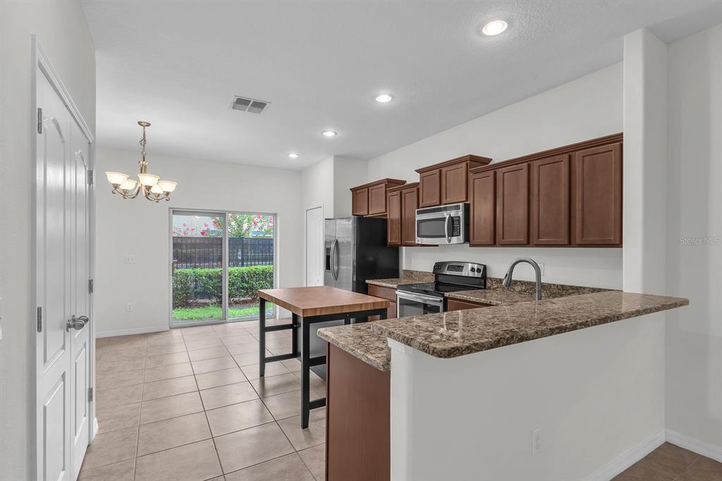 A kitchen features brown cabinets, granite countertops, a center island, and a sliding glass door — 2719 LANTERN HILL AVENUE, BRANDON, FL