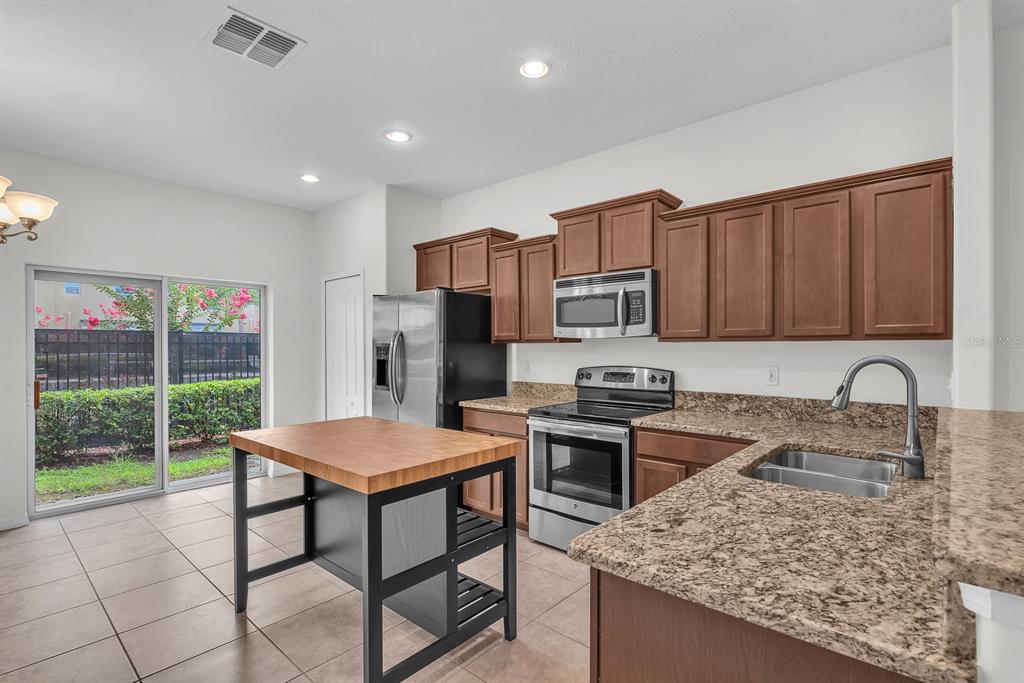 A kitchen features brown cabinets, granite countertops, stainless steel appliances, and a wooden kitchen island — 2719 LANTERN HILL AVENUE, BRANDON, FL