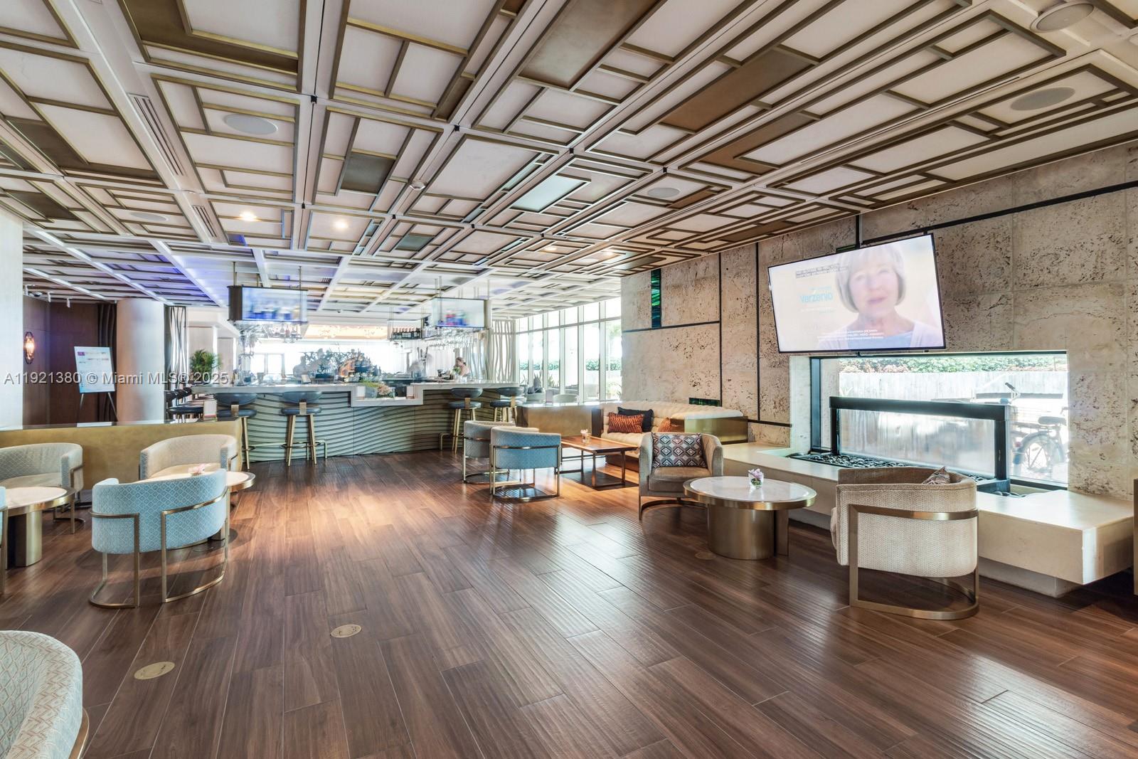 A modern lounge area features wood flooring, a geometric ceiling, a fireplace, and bar seating — 6801 Collins Ave # 320, Miami Beach FL 33141, MIAMI BEACH, FL