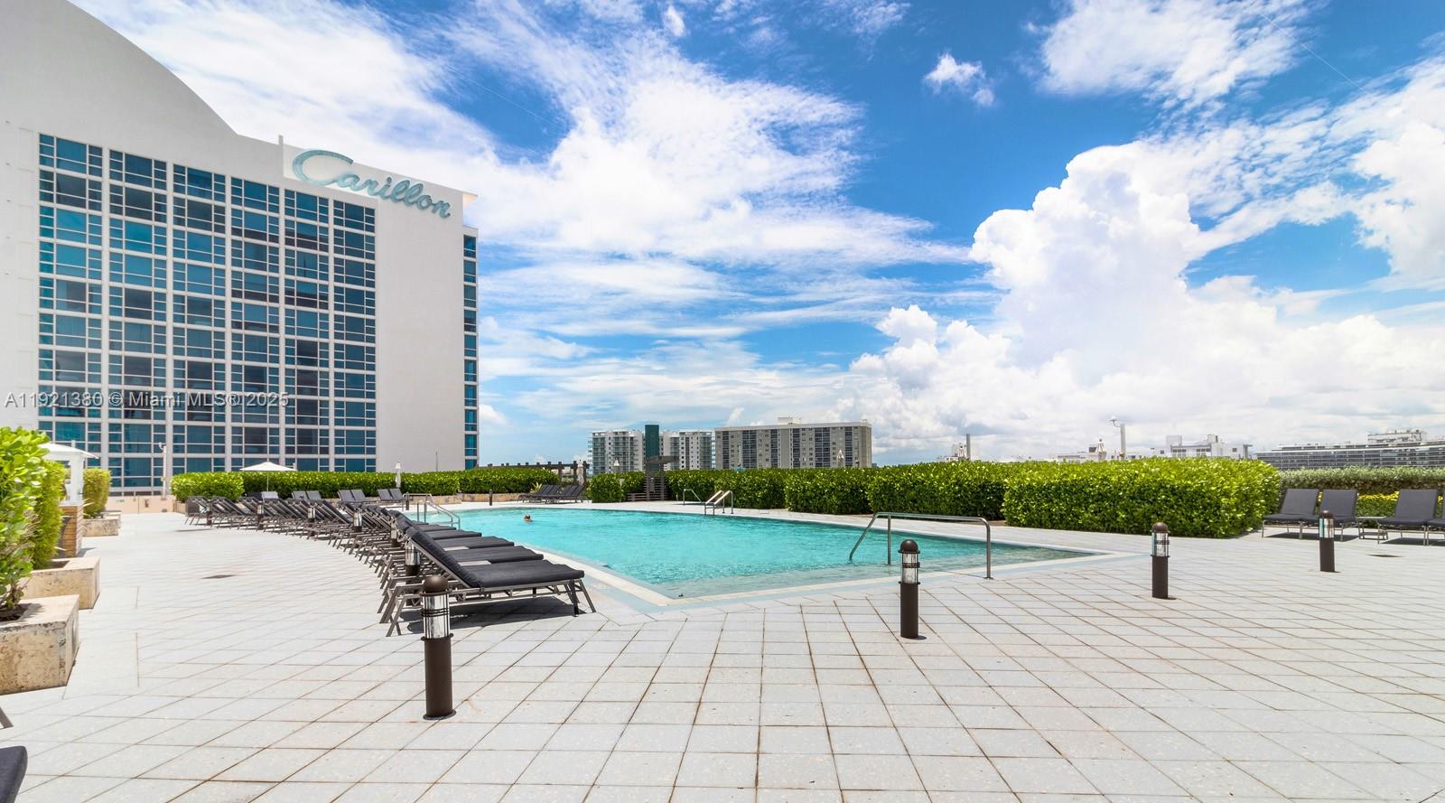 An outdoor swimming pool is surrounded by lounge chairs and a hedge on a patio — 6801 Collins Ave # 320, Miami Beach FL 33141, MIAMI BEACH, FL