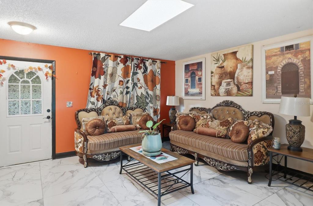 A living room features orange walls, two ornate sofas, a coffee table, and tiled floors — 1736 NW 26TH PLACE, OCALA, FL