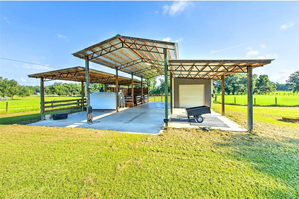 A large, open-sided metal pole barn with a concrete floor sits in a grassy field — 16520 SPRING VALLEY ROAD, DADE CITY, FL
