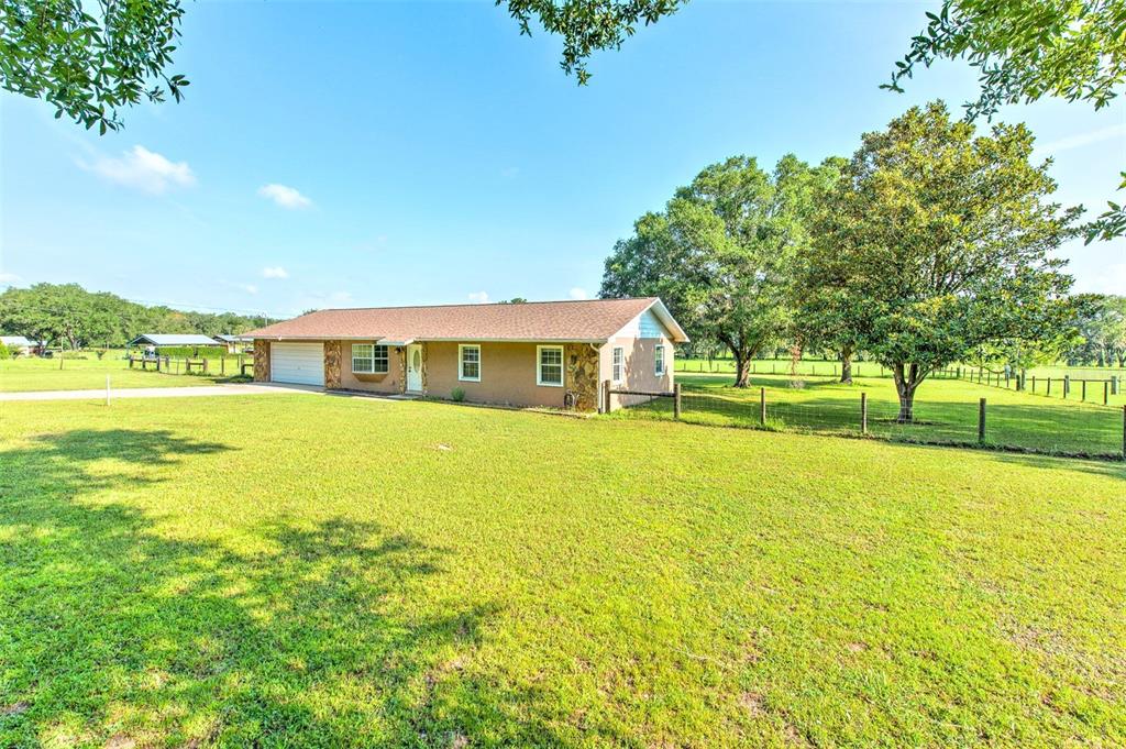 A single-story ranch-style house with a stone facade sits on a large, grassy lot — 16520 SPRING VALLEY ROAD, DADE CITY, FL