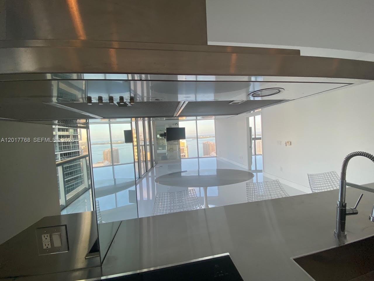 A modern kitchen with stainless steel countertops overlooks a dining area with floor-to-ceiling windows — 495 Brickell Ave # 2902, Miami FL 33131, MIAMI, FL