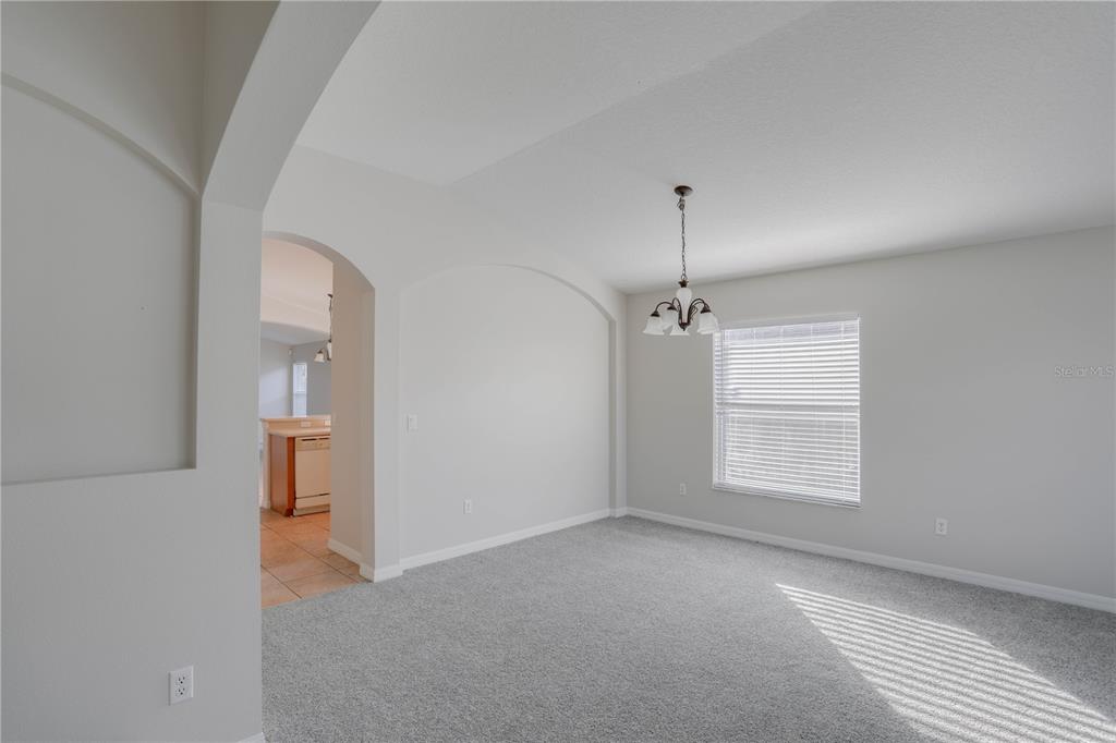 A carpeted dining room features an arched wall cutout, a chandelier, and a window — 9983 BRODBECK BOULEVARD, ORLANDO, FL