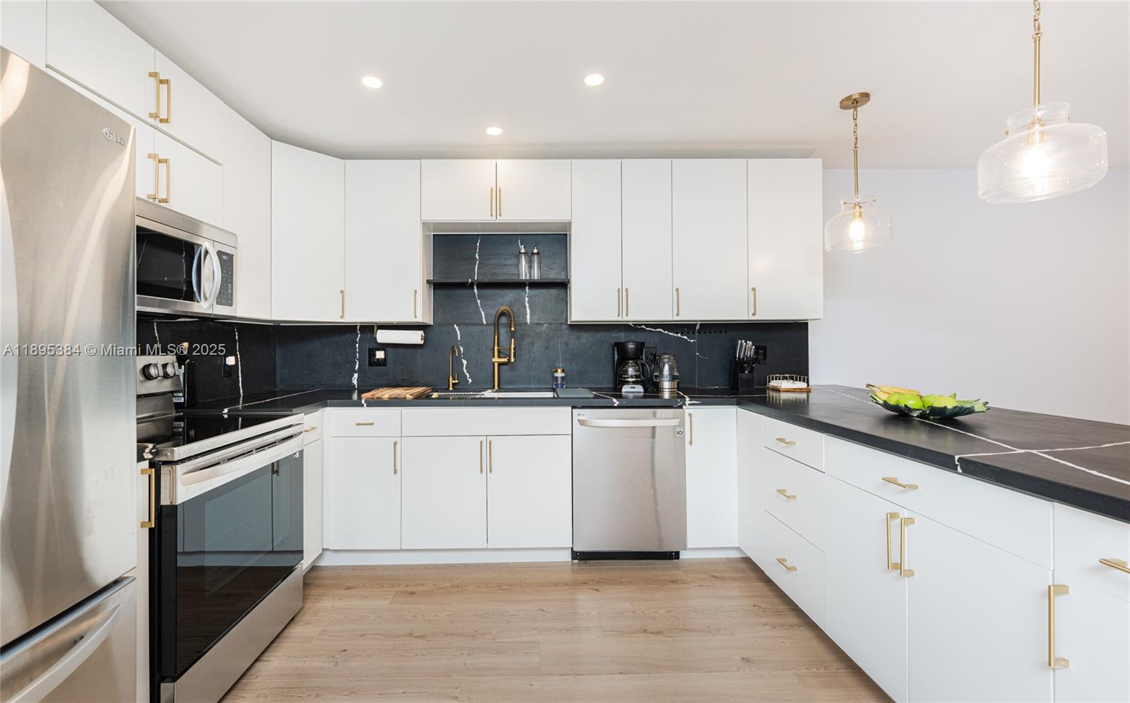 A modern kitchen features white cabinets, black countertops, a black backsplash, and stainless steel appliances — 600 Three Islands Blvd # 214, Hallandale Beach FL 33009, HALLANDALE BEACH, FL