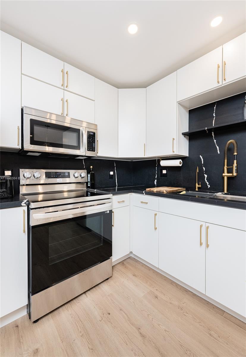 A modern kitchen features white cabinets, stainless steel appliances, and a black marble-patterned backsplash — 600 Three Islands Blvd # 214, Hallandale Beach FL 33009, HALLANDALE BEACH, FL
