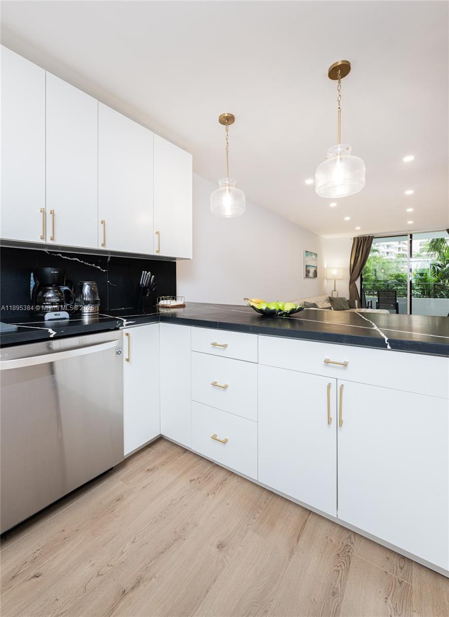 A modern kitchen features white cabinets, black countertops, and stainless steel appliances — 600 Three Islands Blvd # 214, Hallandale Beach FL 33009, HALLANDALE BEACH, FL