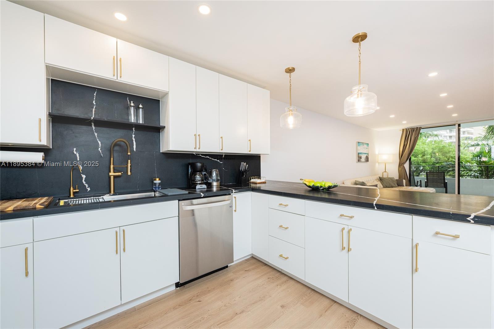 A modern kitchen features white cabinets, black marble countertops, and gold hardware — 600 Three Islands Blvd # 214, Hallandale Beach FL 33009, HALLANDALE BEACH, FL