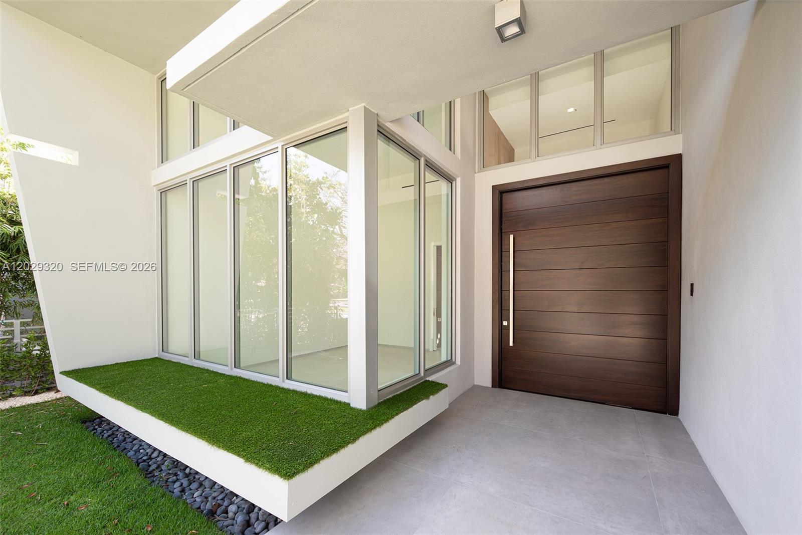 A modern entryway features a large wood door, floor-to-ceiling glass windows, and artificial grass landscaping — 2100 S Miami Ave, Miami FL 33129, MIAMI, FL