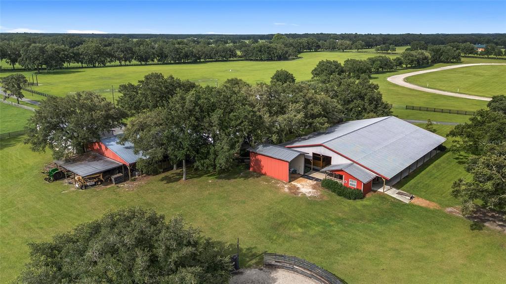 An aerial view shows two red barns surrounded by green pastures and mature oak trees — 18800 SE 47TH PLACE, MORRISTON, FL
