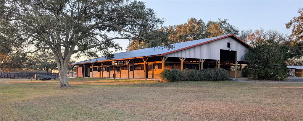 A long, metal-roofed horse stable with wooden stalls sits on a grassy field — 18800 SE 47TH PLACE, MORRISTON, FL