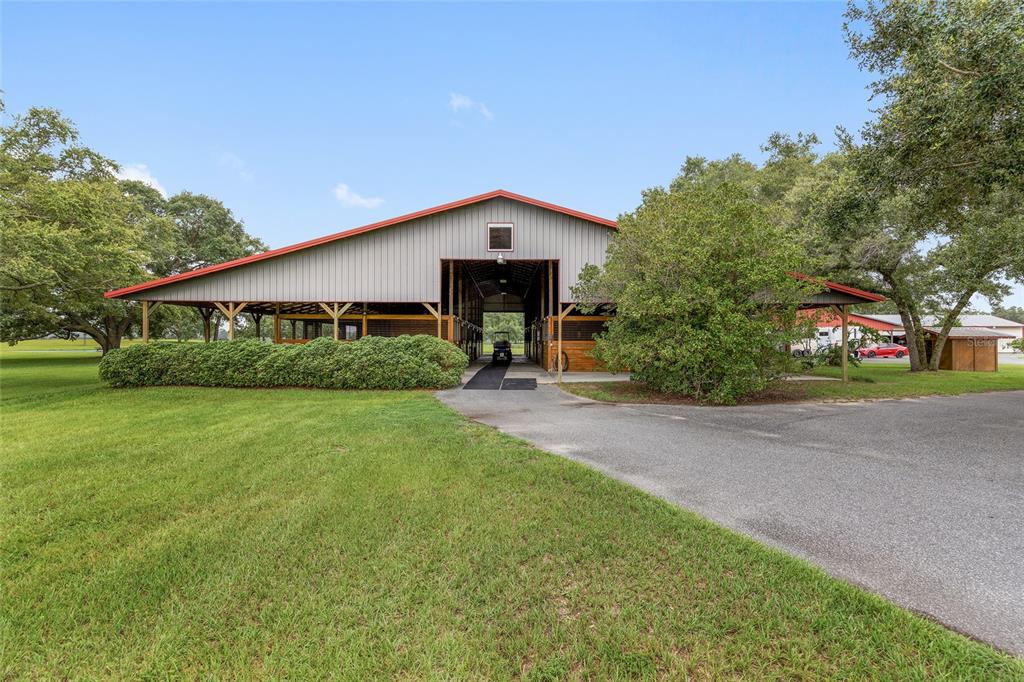 A large metal-sided horse barn with a central breezeway stands on a grassy lot — 18800 SE 47TH PLACE, MORRISTON, FL