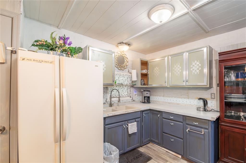 A kitchen features blue lower cabinets, white tiled countertops, and a white side-by-side refrigerator — 3355 SE 92ND STREET, OCALA, FL