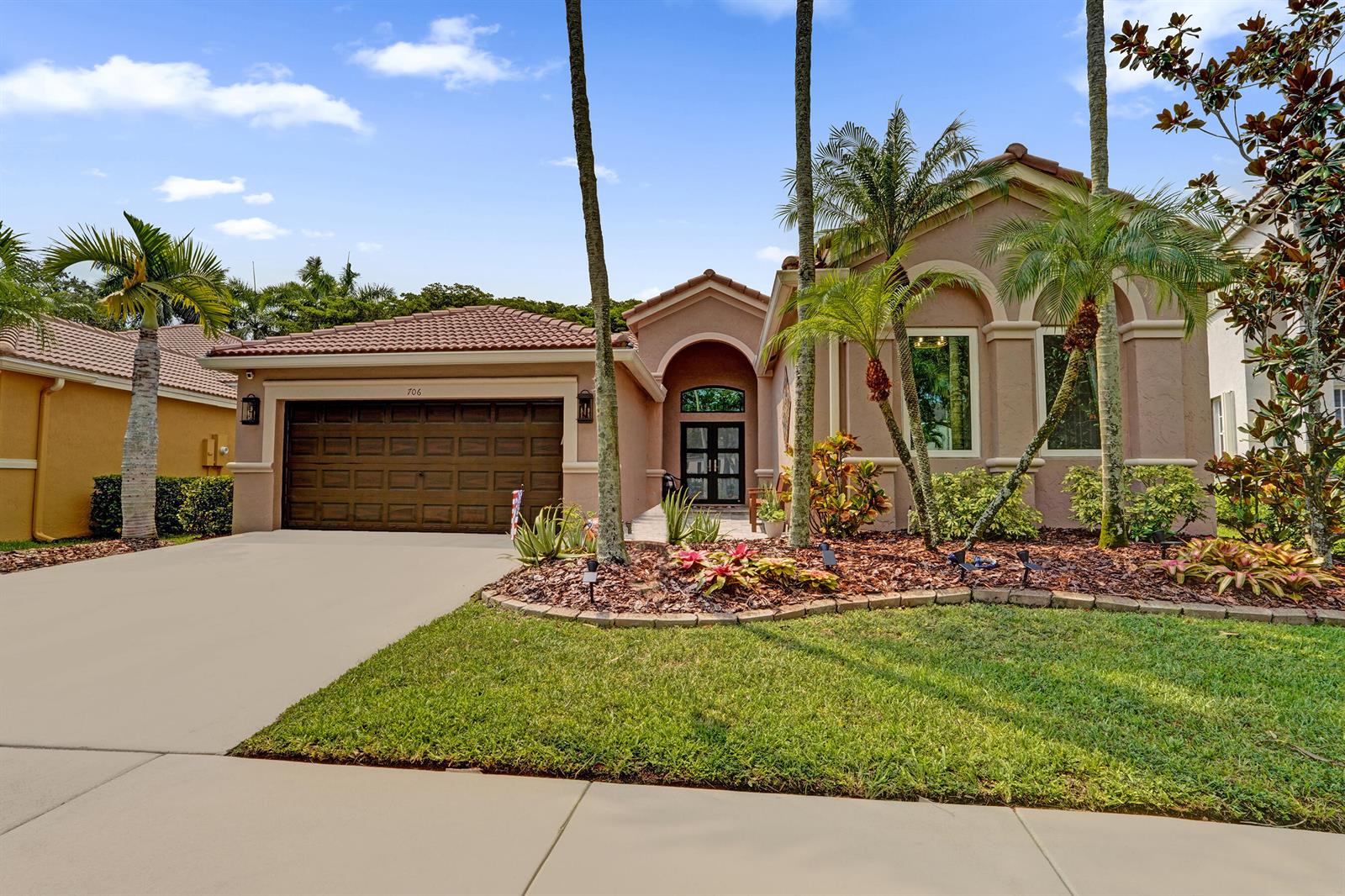 A single-story tan stucco house with a tile roof, two-car garage, and palm trees — 706 Tulip Circle, Weston FL 33327, WESTON, FL