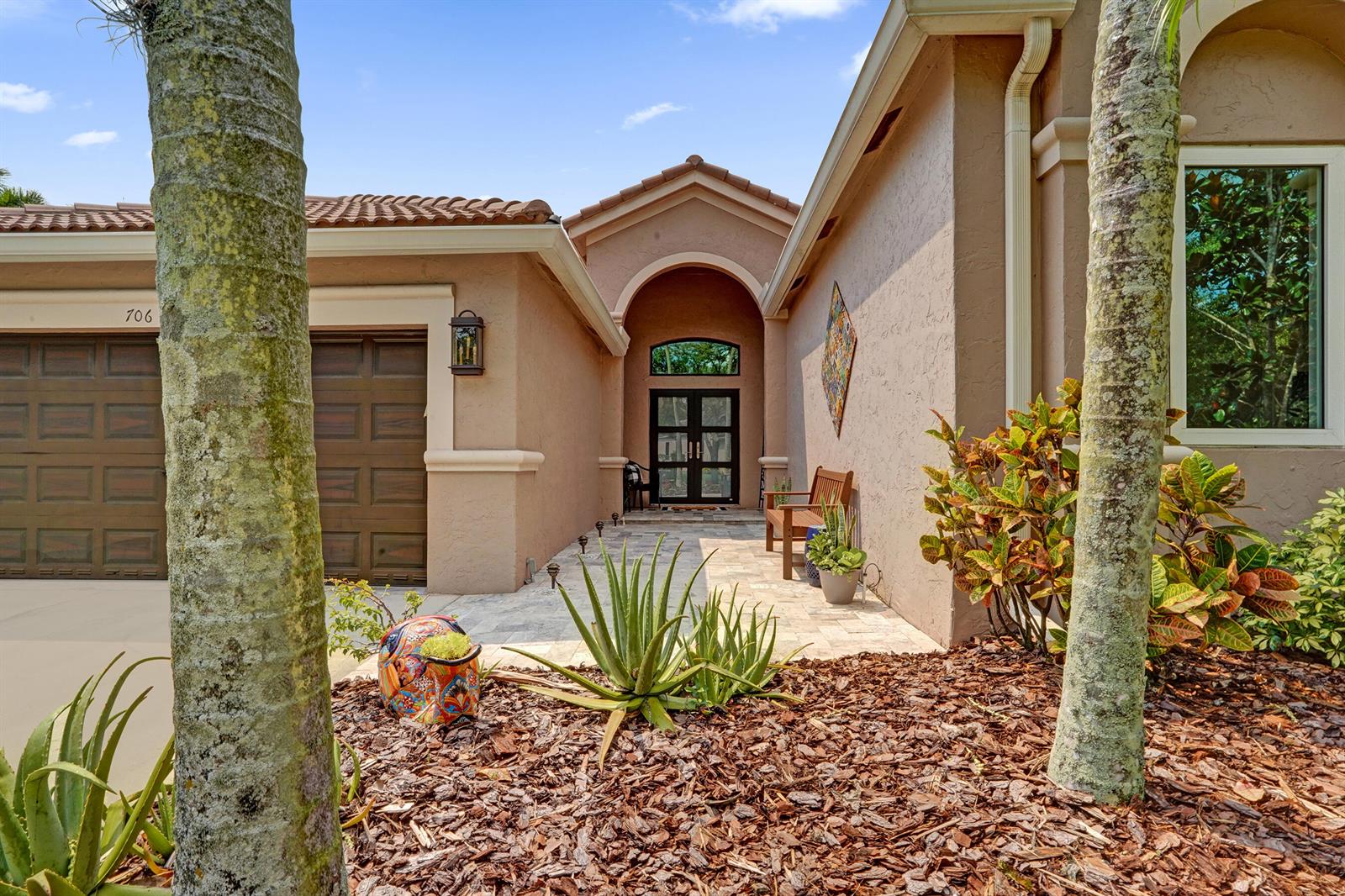The exterior of a tan stucco house features a stone walkway, arched entryway, and palm trees — 706 Tulip Circle, Weston FL 33327, WESTON, FL