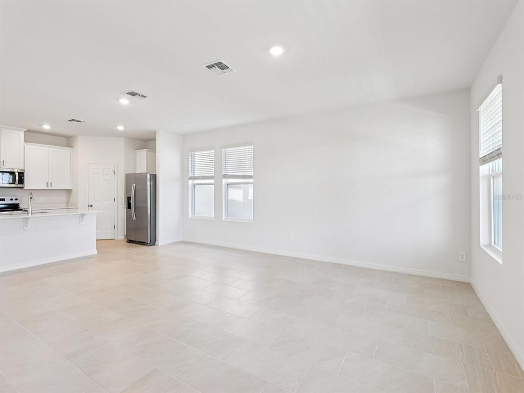 An open-concept kitchen and living area with white cabinets, stainless steel appliances, and tile flooring — 4680 HOMESTEAD TRAIL, ST CLOUD, FL