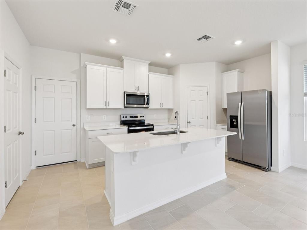 A modern kitchen features white cabinets, stainless steel appliances, and a central island with seating — 4680 HOMESTEAD TRAIL, ST CLOUD, FL