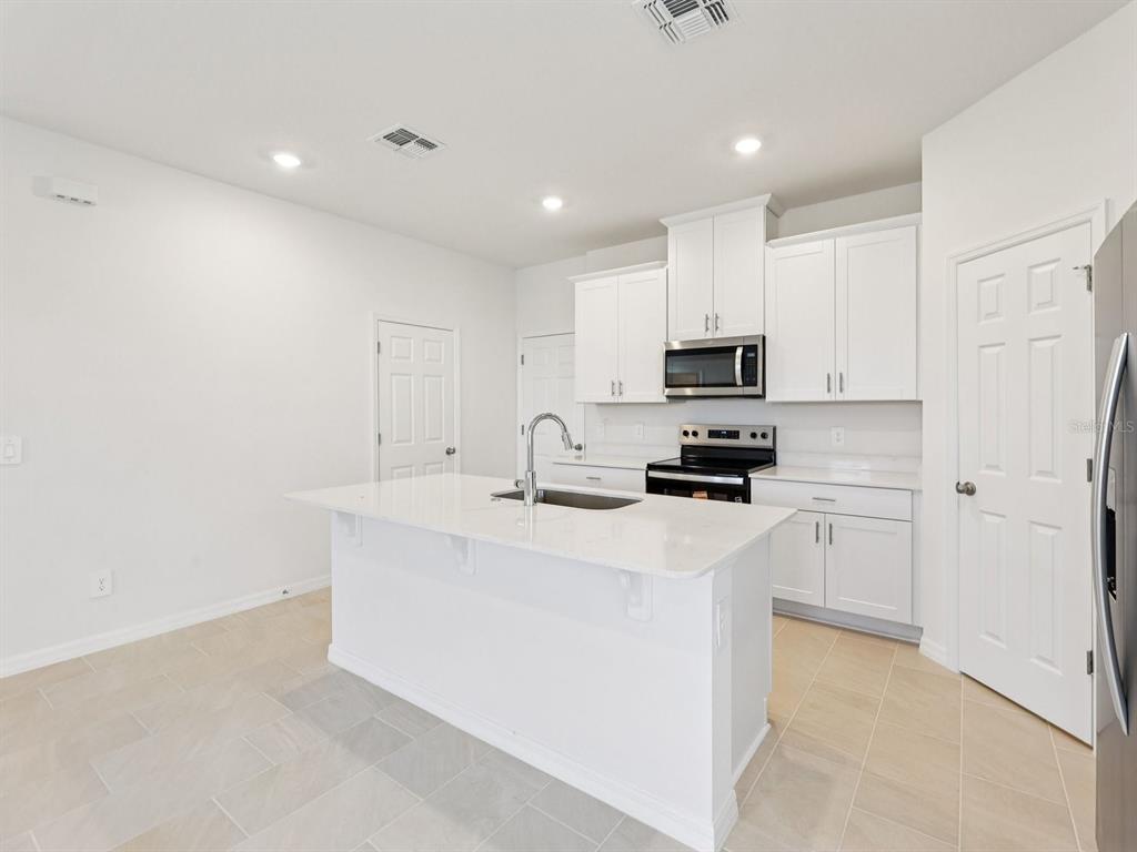 A modern kitchen features white cabinets, a central island with a sink, and tile flooring — 4680 HOMESTEAD TRAIL, ST CLOUD, FL