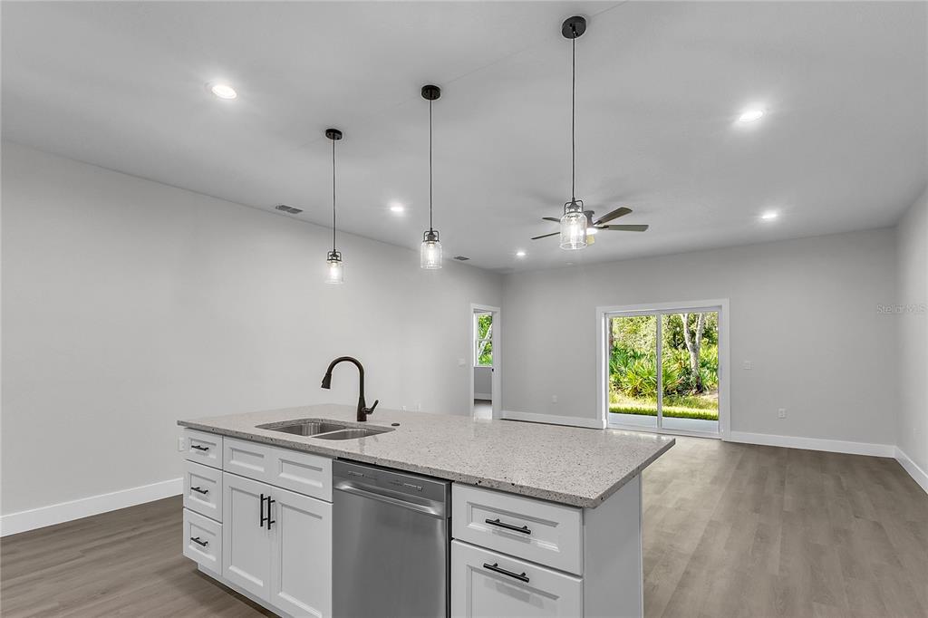A kitchen island with a stainless steel dishwasher and sink sits before an open living area — 6 EASTON PLACE, PALM COAST, FL