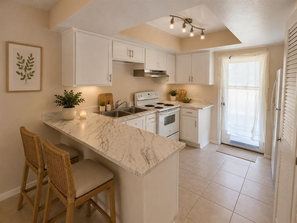 A kitchen features white cabinets, marble-look countertops, a breakfast bar with two stools, and tile flooring — 29 W COUNTRY COVE WAY UNIT 29, KISSIMMEE, FL