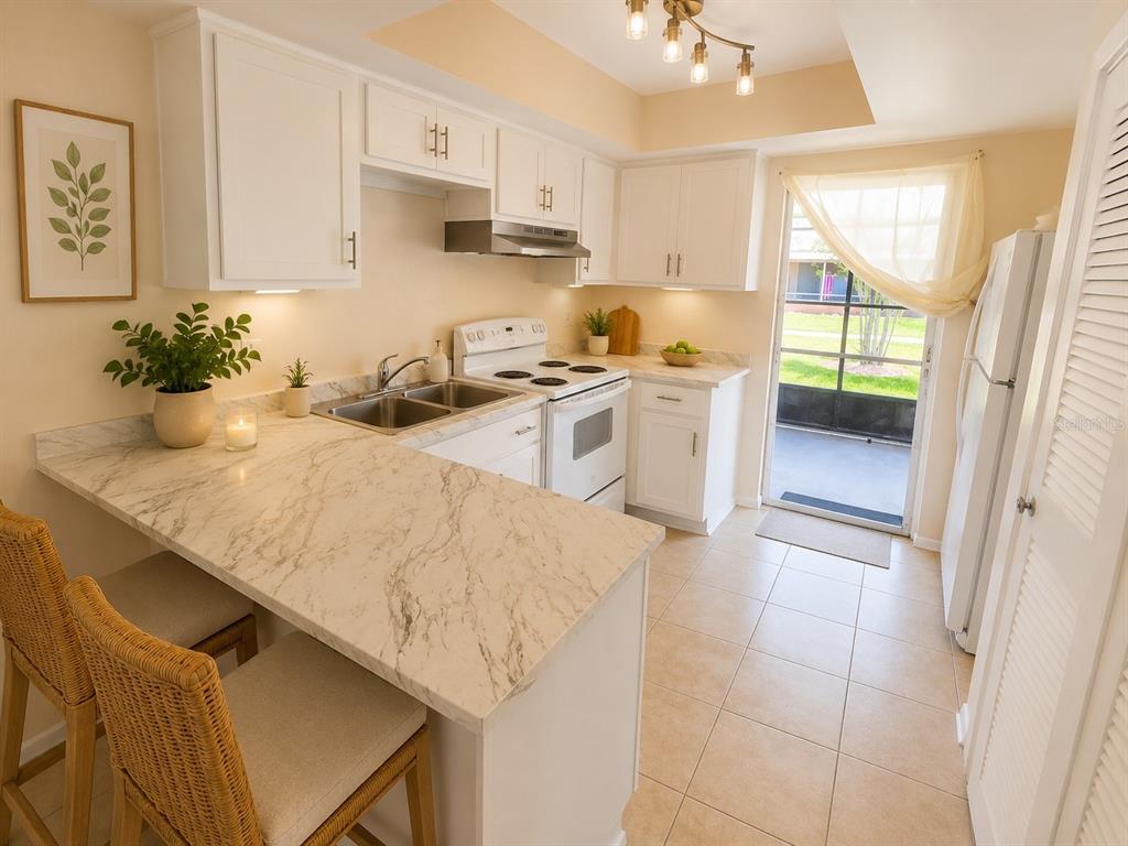 A bright kitchen features white cabinets, marble-look countertops, a breakfast bar, and a sliding door — 29 W COUNTRY COVE WAY UNIT 29, KISSIMMEE, FL