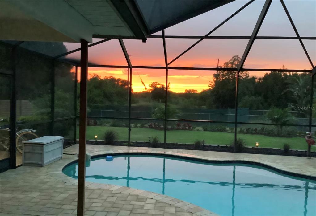 A swimming pool sits on a patio enclosed by a screen cage at sunset — 5916 OAKHURST DRIVE, SEMINOLE, FL