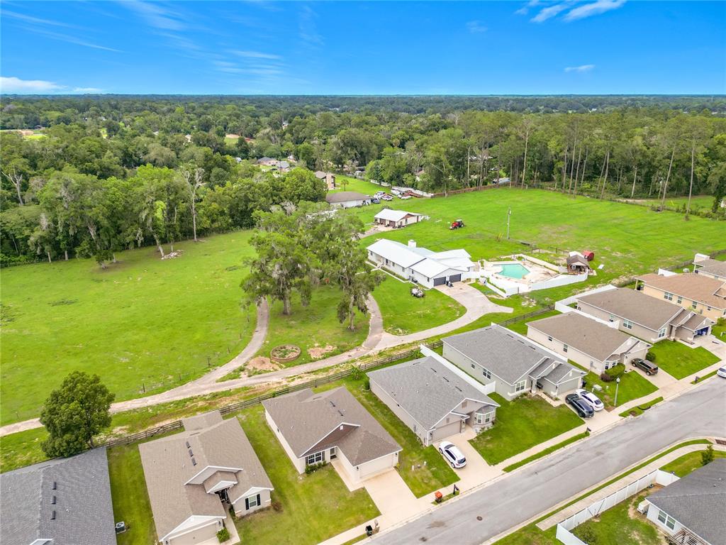 An aerial view shows a residential neighborhood bordering a large, open green pasture — 187 NW 45TH LOOP, OCALA, FL