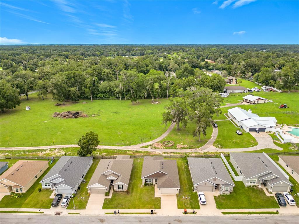An aerial view shows a row of suburban houses bordering a large, open grassy field — 187 NW 45TH LOOP, OCALA, FL