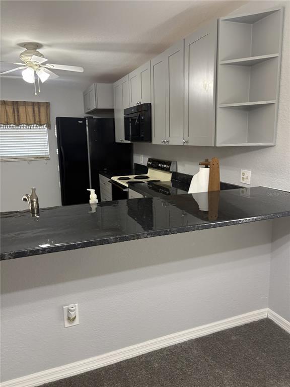 A kitchen features gray cabinets, a black countertop, and a black refrigerator — 175 KINGS HIGHWAY UNIT A1, PUNTA GORDA, FL