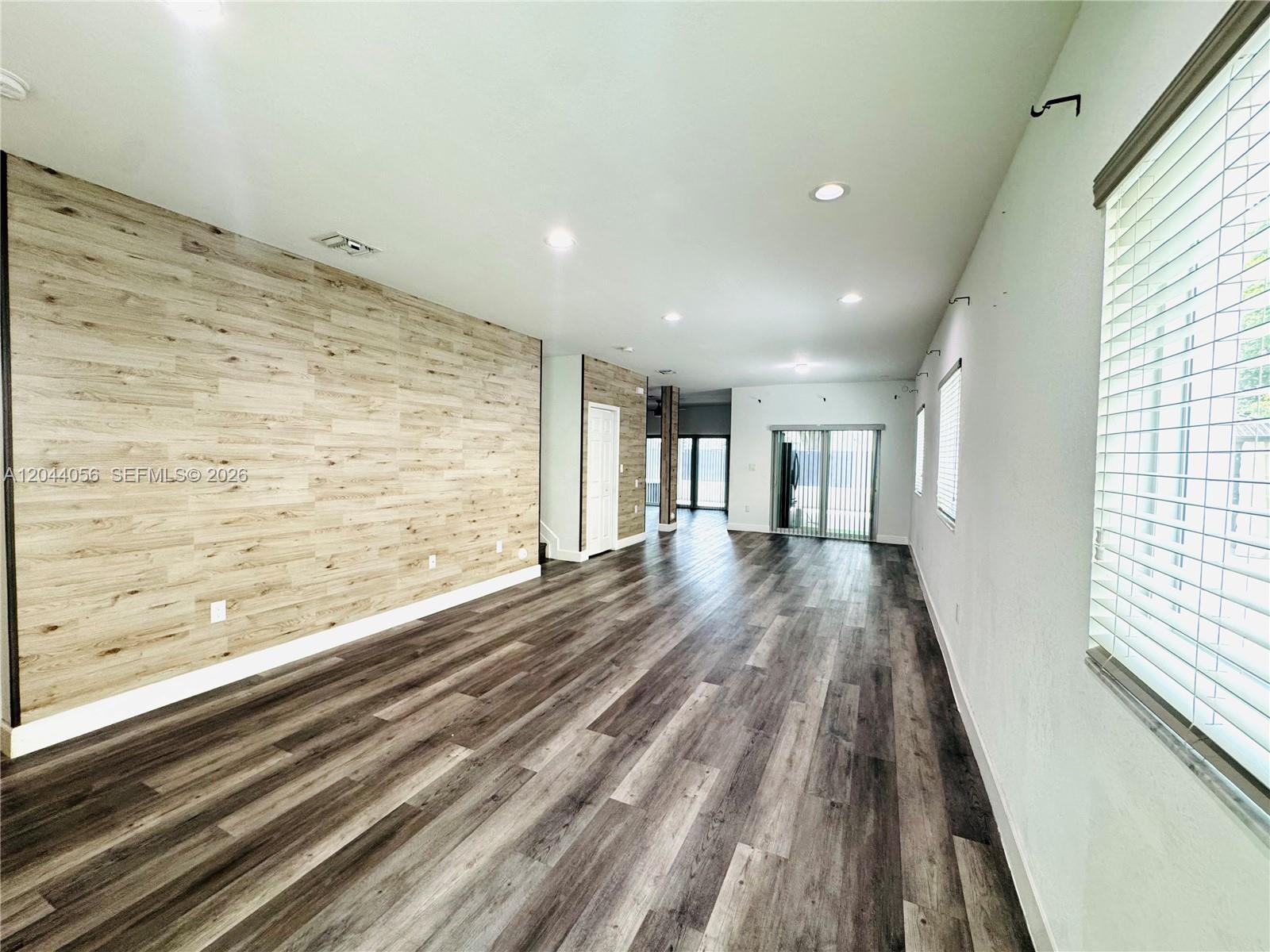 An open living area features wood-look plank flooring and a light wood-paneled accent wall — 363 NE 35th Ter, Homestead FL 33033, HOMESTEAD, FL