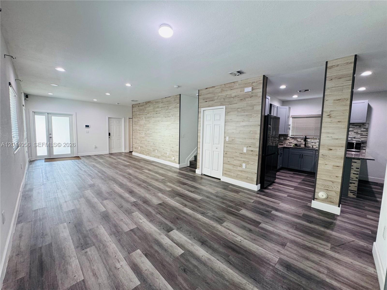 A living area with wood-look flooring and accent walls leads into a modern kitchen — 363 NE 35th Ter, Homestead FL 33033, HOMESTEAD, FL