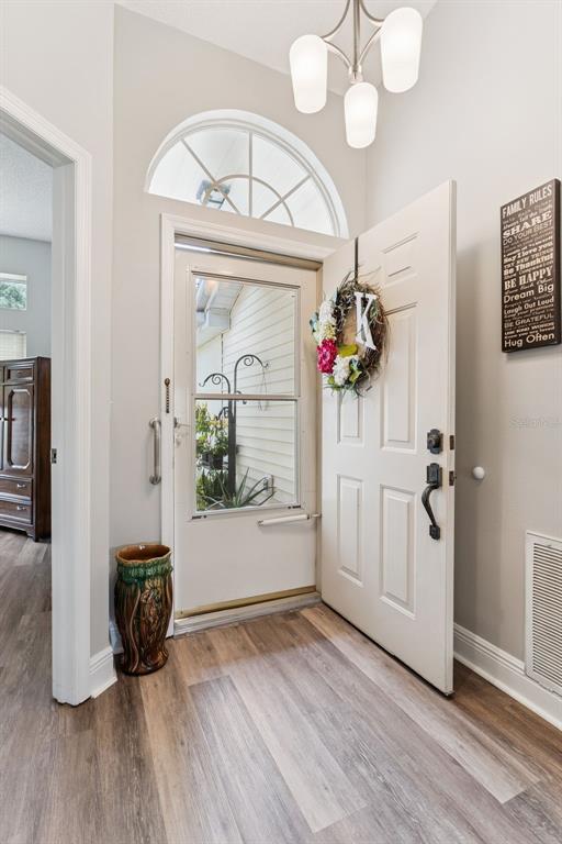 An entryway features a white front door with a glass storm door and wood-look flooring — 2404 NANTUCKET GLEN PLACE UNIT 2404, SUN CITY CENTER, FL