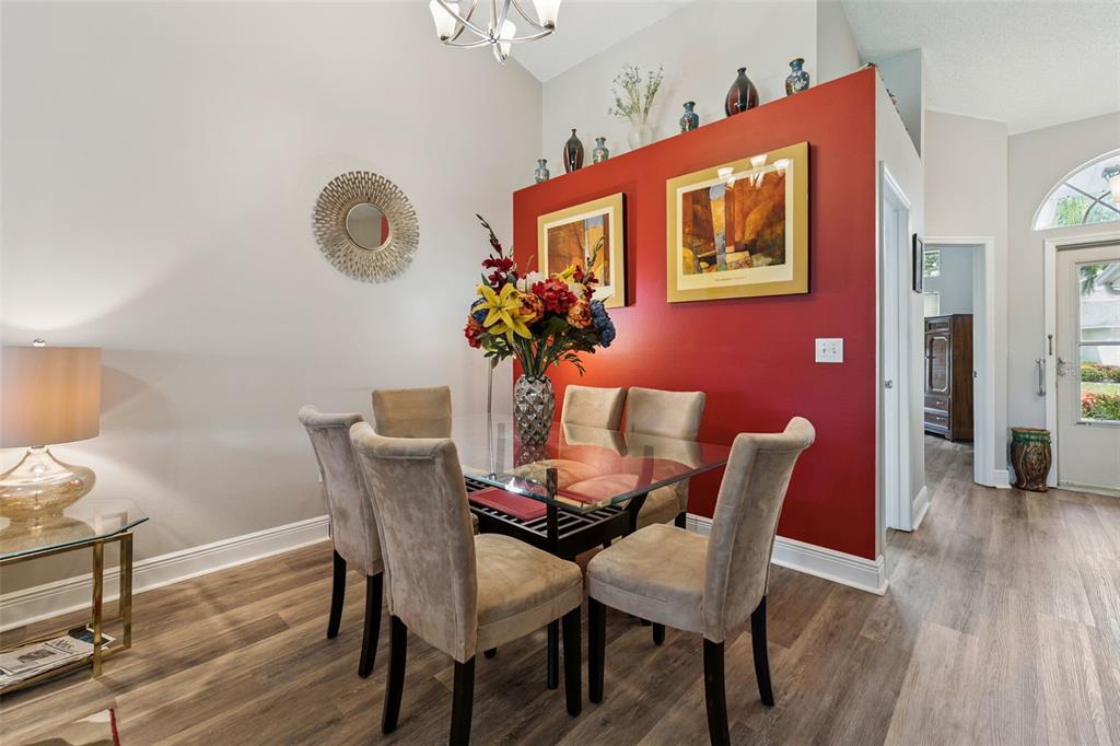 A dining room features a glass table, beige chairs, and a red accent wall — 2404 NANTUCKET GLEN PLACE UNIT 2404, SUN CITY CENTER, FL