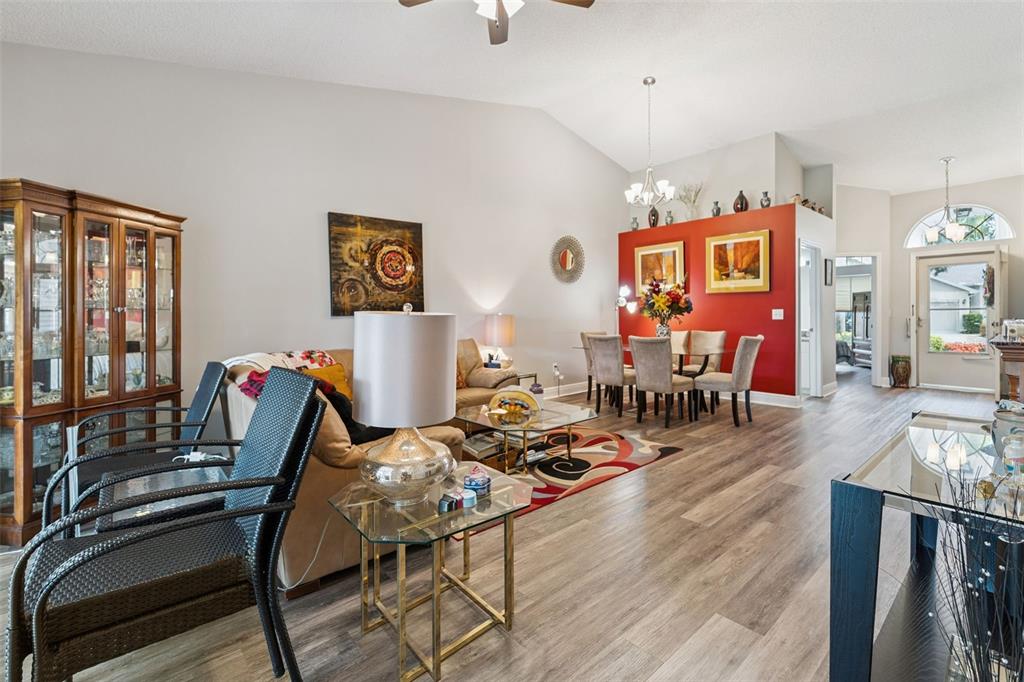 A living and dining area features wood-look flooring, a red accent wall, and vaulted ceilings — 2404 NANTUCKET GLEN PLACE UNIT 2404, SUN CITY CENTER, FL