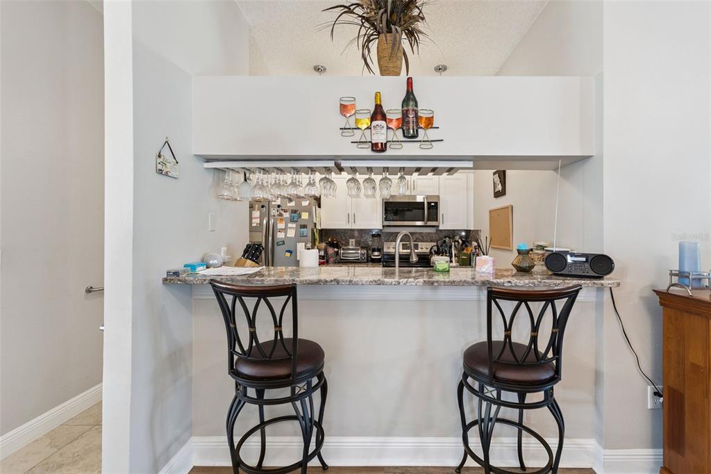 A kitchen pass-through features a granite breakfast bar with two stools and hanging glassware — 2404 NANTUCKET GLEN PLACE UNIT 2404, SUN CITY CENTER, FL