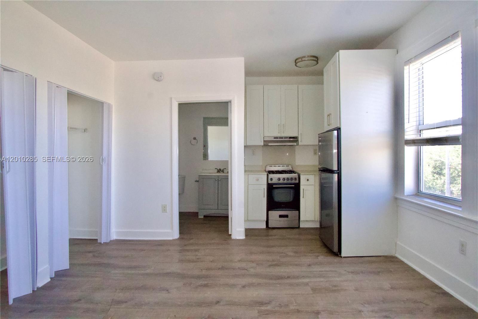 A small kitchen with white cabinets and stainless steel appliances sits beside a bathroom doorway — 501 SW 6th Ct # 322, Miami FL 33130, MIAMI, FL
