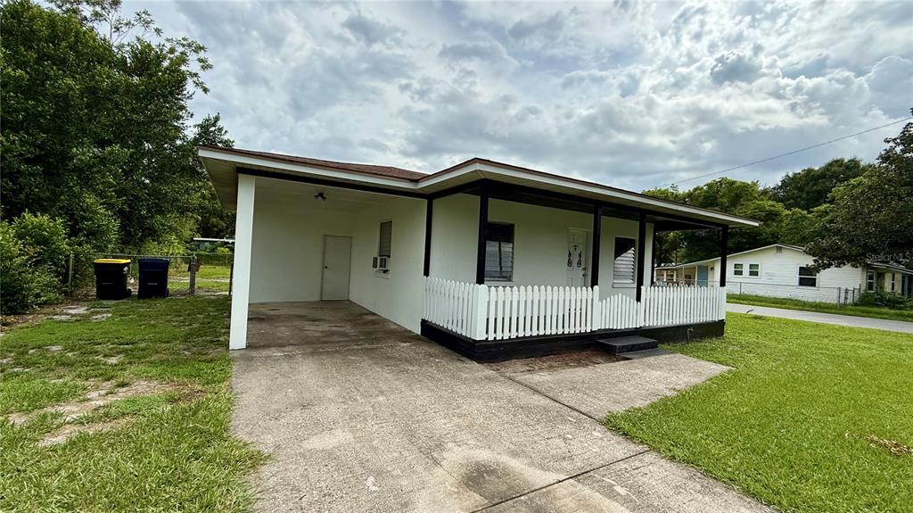 A white house with a covered carport, a front porch, and a white picket fence — 202 E POLK STREET, AUBURNDALE, FL