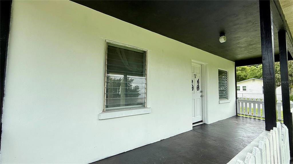 A covered front porch with a white exterior wall, a door, and a white picket fence — 202 E POLK STREET, AUBURNDALE, FL