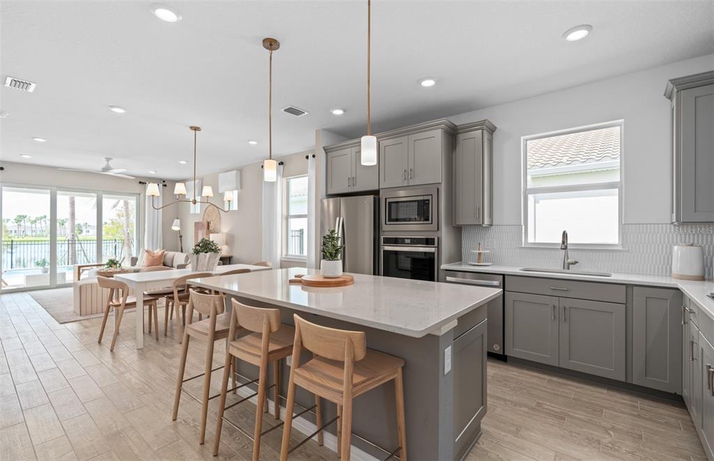 A modern kitchen with gray cabinets, a quartz island, and wood-look tile flooring — 6760 SUNRISE COVE DRIVE, CLERMONT, FL