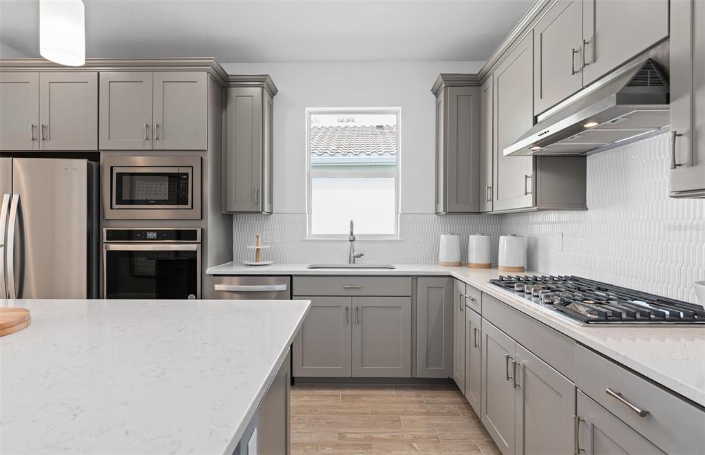 A modern kitchen features gray cabinets, white quartz countertops, stainless steel appliances, and tile flooring — 6760 SUNRISE COVE DRIVE, CLERMONT, FL