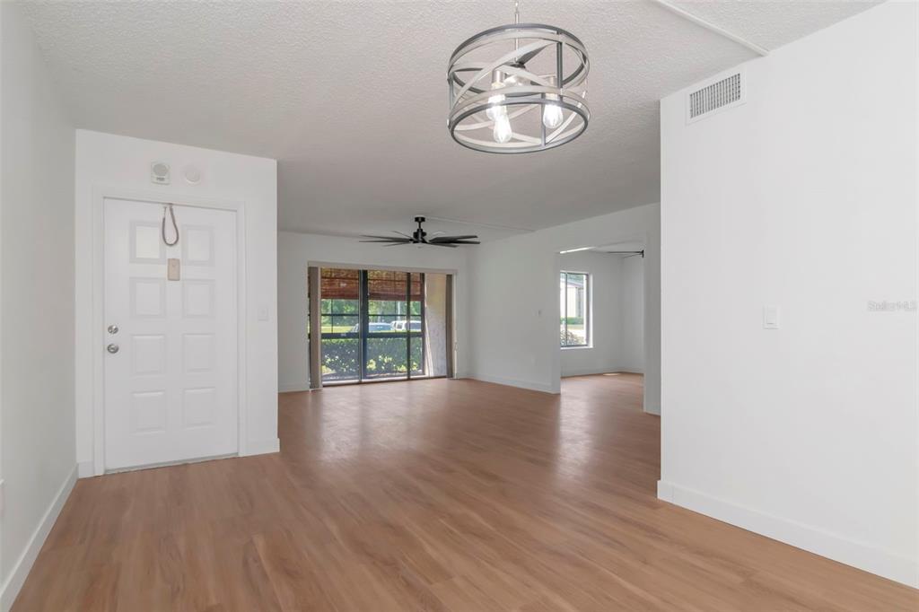 An empty living room features light wood-look flooring, white walls, and a modern drum chandelier — 3211 LAKE PINE WAY E UNIT A1, TARPON SPRINGS, FL