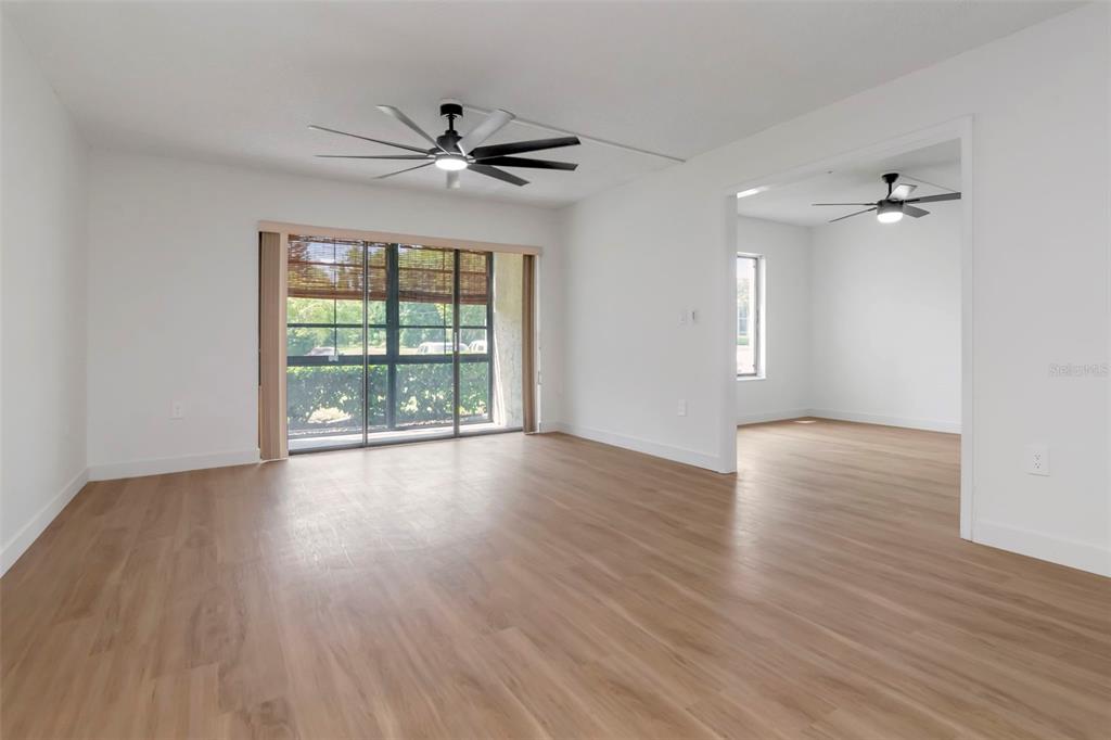An empty living room with light wood-look flooring, white walls, and two ceiling fans — 3211 LAKE PINE WAY E UNIT A1, TARPON SPRINGS, FL