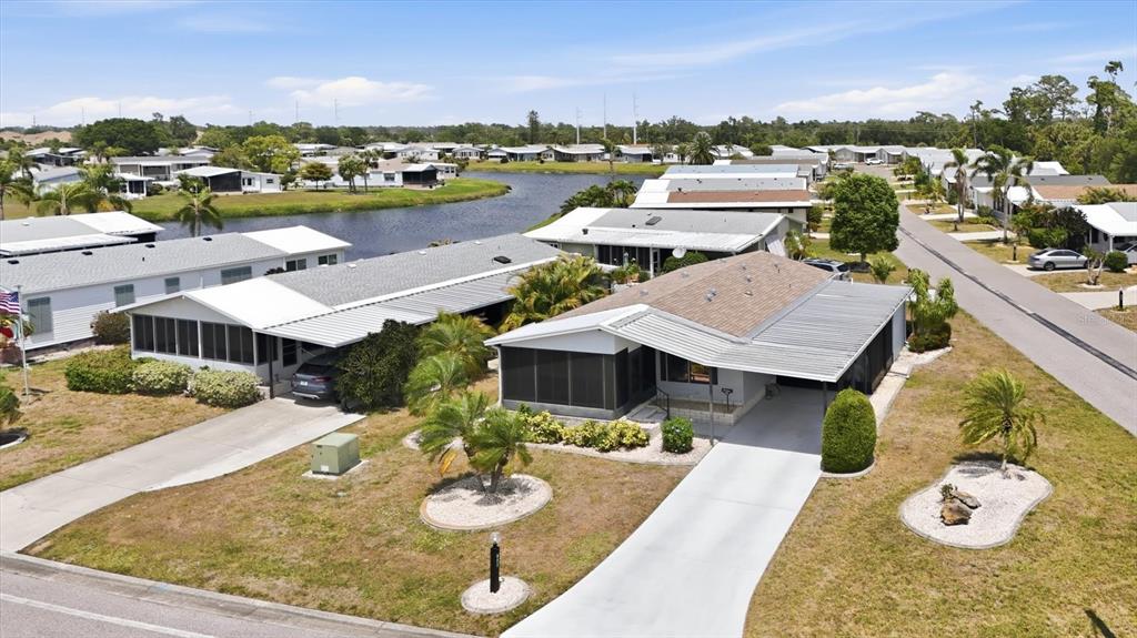 An aerial view shows two adjacent manufactured homes with driveways and carports near a lake — 803 TANGERINE WOODS BOULEVARD, ENGLEWOOD, FL