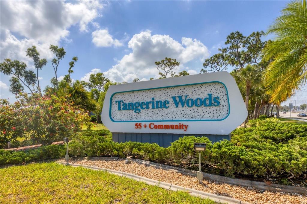 A sign for Tangerine Woods 55+ Community stands in a landscaped area with trees — 803 TANGERINE WOODS BOULEVARD, ENGLEWOOD, FL