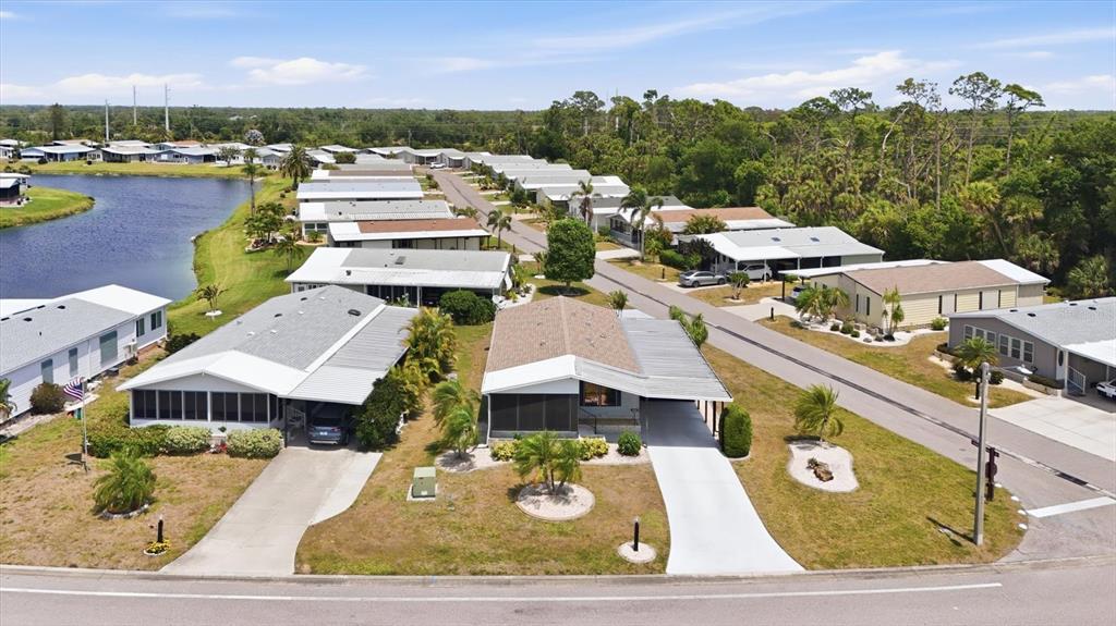 An aerial view shows several manufactured homes with driveways and carports near a small lake — 803 TANGERINE WOODS BOULEVARD, ENGLEWOOD, FL
