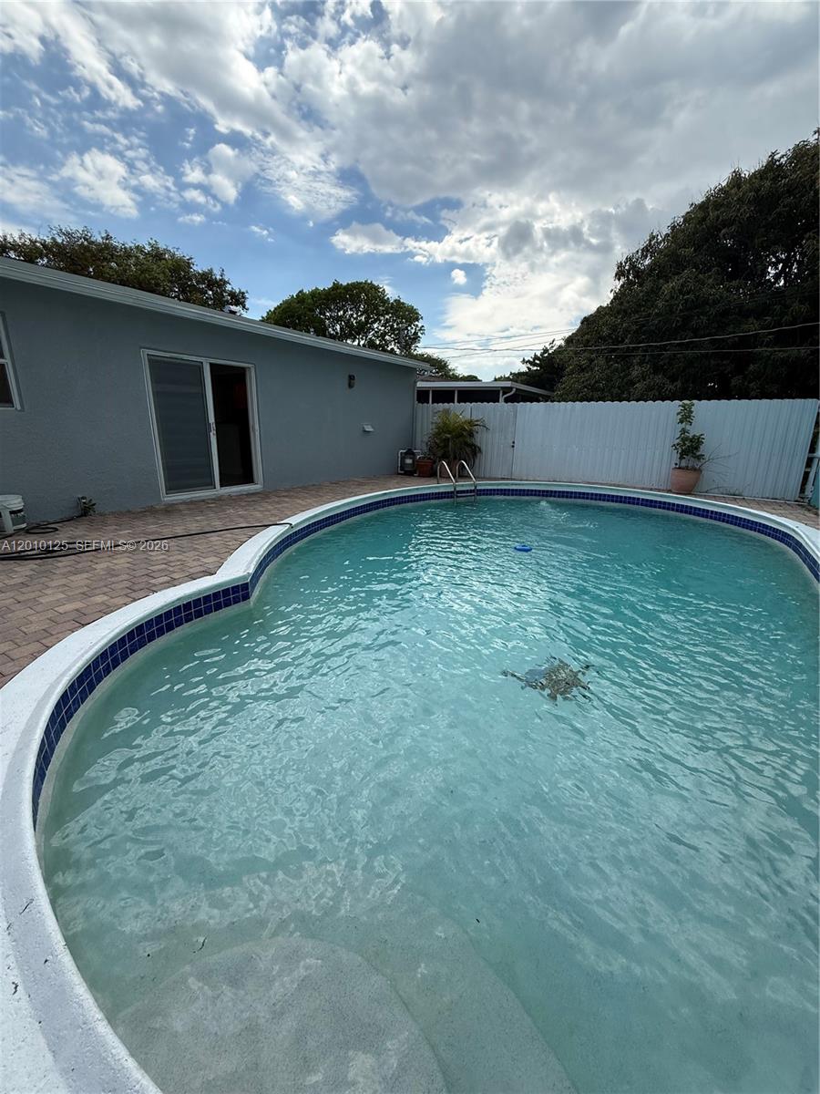 A backyard features a kidney-shaped swimming pool with blue tile trim and a paved patio — 1619 Shenandoah St, Hollywood FL 33020, HOLLYWOOD, FL
